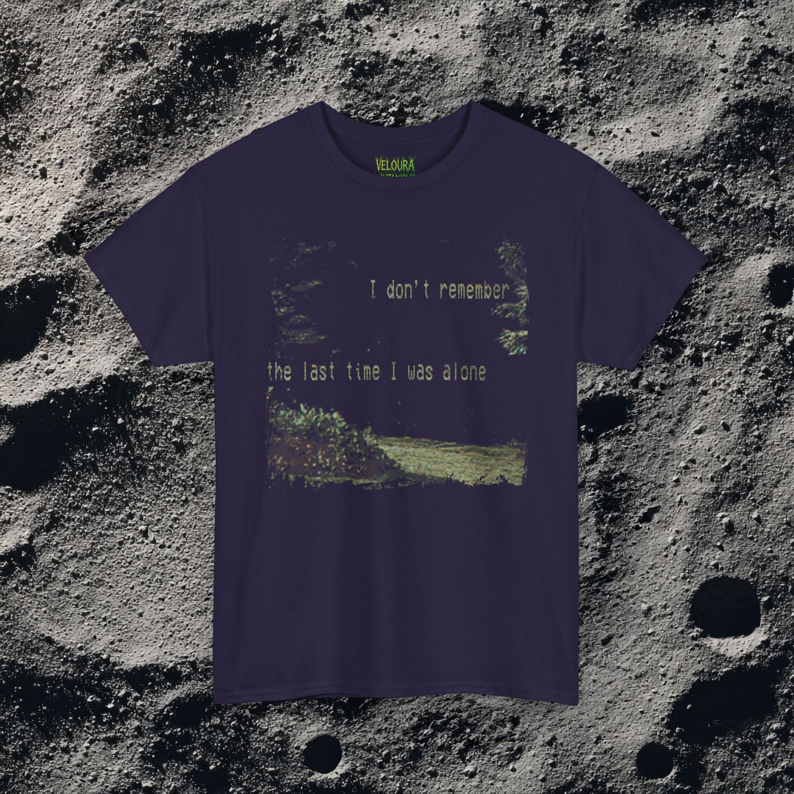t-shirt features a haunting analog horror design, with the front displaying eerie VHS-style forest imagery and glitch effects alongside the unsettling text “I don’t remember the last time I was alone,” while the back shows a grainy night scene of tall grass and trees with a distorted, skeletal humanoid creature leaning forward and staring with a wide grin, accompanied by the chilling phrase “It never lets me out of sight,” creating a disturbing and atmospheric look that captures the feeling of being stalked and never truly alone.