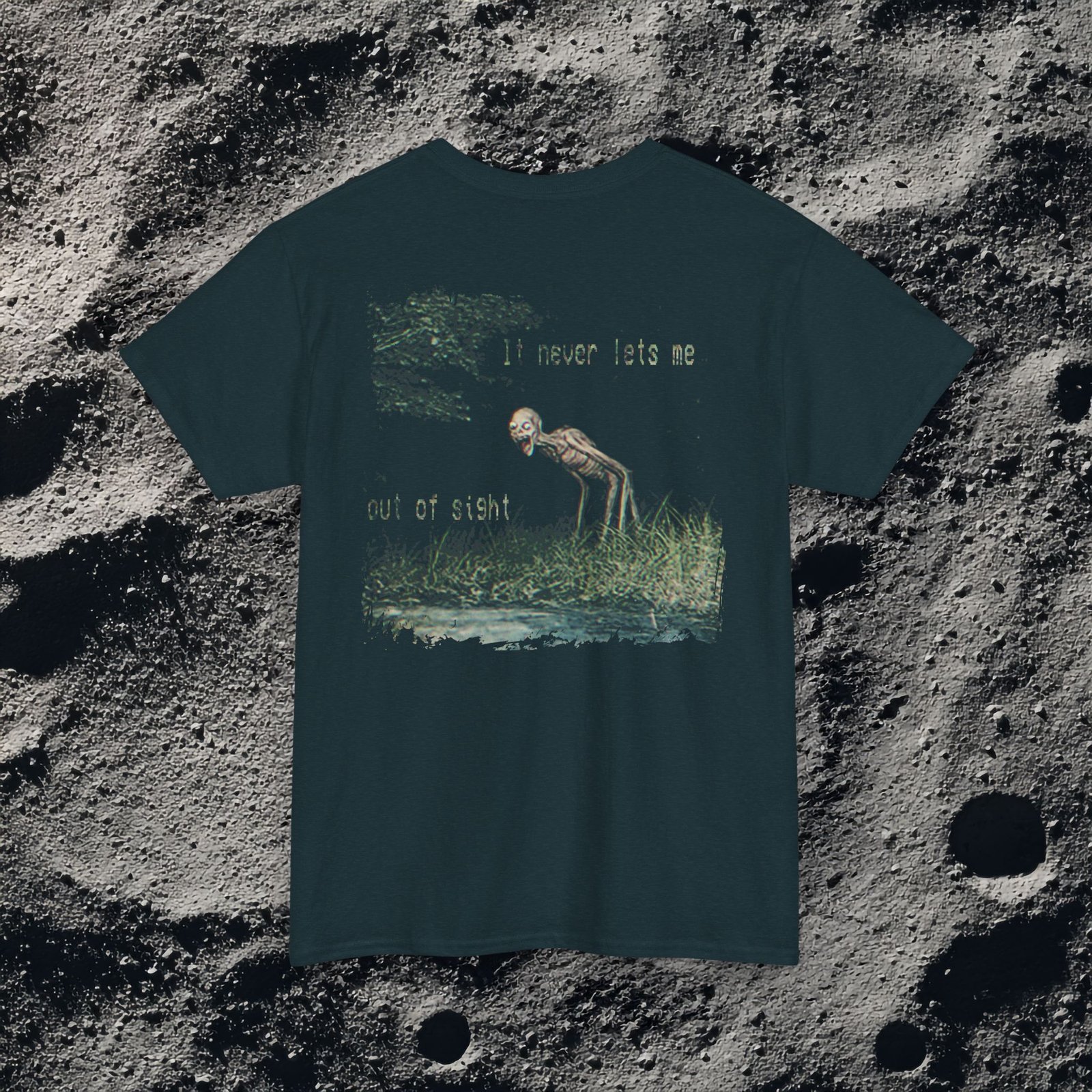 t-shirt features a haunting analog horror design, with the front displaying eerie VHS-style forest imagery and glitch effects alongside the unsettling text “I don’t remember the last time I was alone,” while the back shows a grainy night scene of tall grass and trees with a distorted, skeletal humanoid creature leaning forward and staring with a wide grin, accompanied by the chilling phrase “It never lets me out of sight,” creating a disturbing and atmospheric look that captures the feeling of being stalked and never truly alone.
