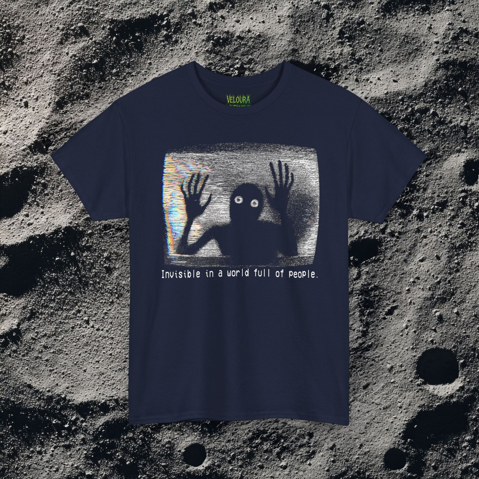 This black T-shirt features an analog horror inspired design of a grainy, distorted humanoid silhouette trapped inside a static-filled television screen. The shadowy figure presses its long, bony hands against the glass as if trying to escape, while its glowing white eyes stare outward in a mix of fear and desperation. VHS-style static and rainbow glitch streaks fill the background, giving the design the appearance of a corrupted video frame. Beneath the image, in a pixelated glitch font, the text reads “Invisible in a world full of people,” adding a dark, emotional layer of loneliness and isolation to the already unsettling graphic.