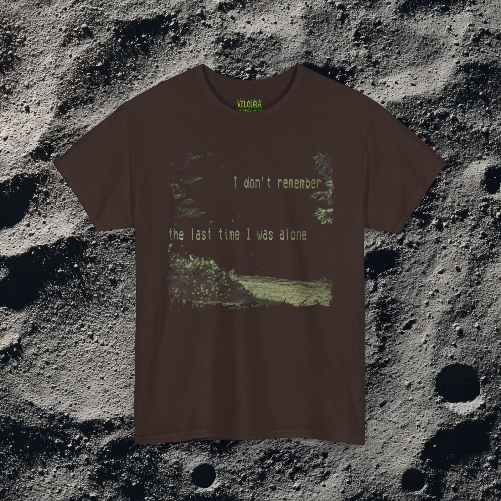 t-shirt features a haunting analog horror design, with the front displaying eerie VHS-style forest imagery and glitch effects alongside the unsettling text “I don’t remember the last time I was alone,” while the back shows a grainy night scene of tall grass and trees with a distorted, skeletal humanoid creature leaning forward and staring with a wide grin, accompanied by the chilling phrase “It never lets me out of sight,” creating a disturbing and atmospheric look that captures the feeling of being stalked and never truly alone.