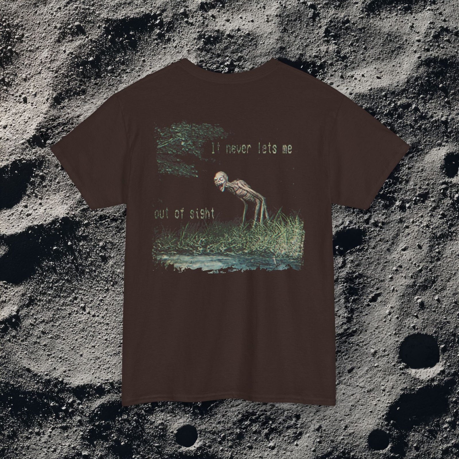 t-shirt features a haunting analog horror design, with the front displaying eerie VHS-style forest imagery and glitch effects alongside the unsettling text “I don’t remember the last time I was alone,” while the back shows a grainy night scene of tall grass and trees with a distorted, skeletal humanoid creature leaning forward and staring with a wide grin, accompanied by the chilling phrase “It never lets me out of sight,” creating a disturbing and atmospheric look that captures the feeling of being stalked and never truly alone.