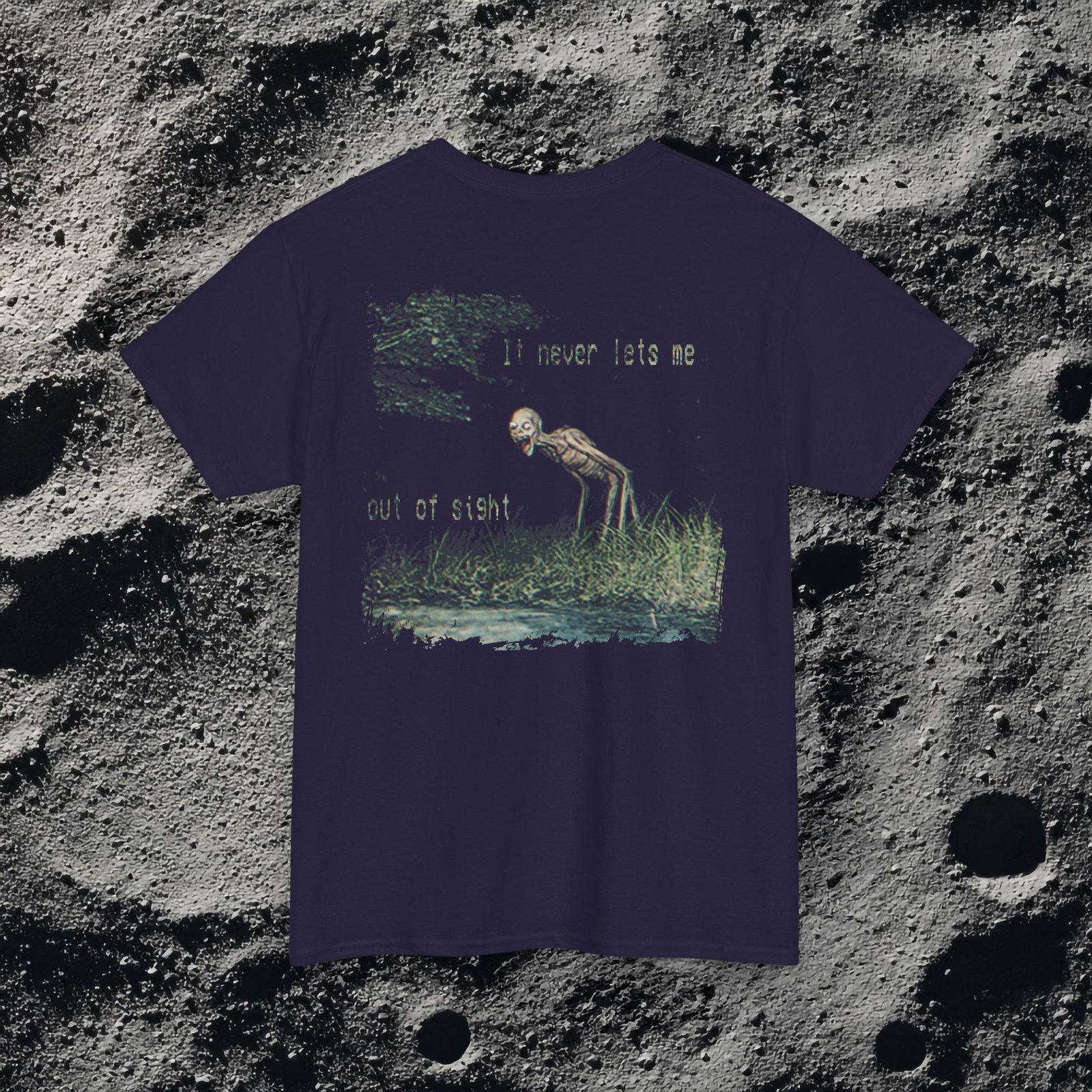 t-shirt features a haunting analog horror design, with the front displaying eerie VHS-style forest imagery and glitch effects alongside the unsettling text “I don’t remember the last time I was alone,” while the back shows a grainy night scene of tall grass and trees with a distorted, skeletal humanoid creature leaning forward and staring with a wide grin, accompanied by the chilling phrase “It never lets me out of sight,” creating a disturbing and atmospheric look that captures the feeling of being stalked and never truly alone.