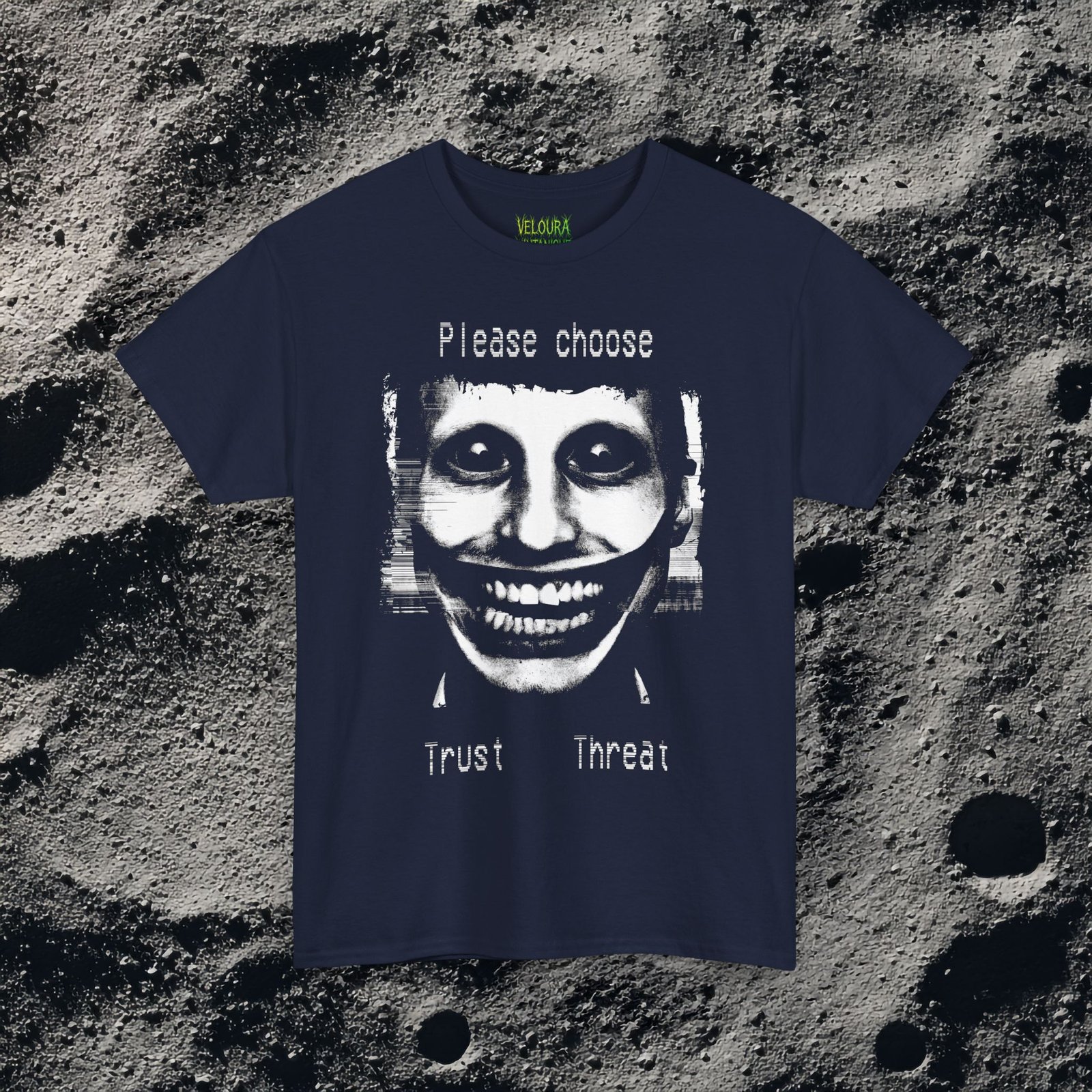 This t-shirt features a disturbing analog horror design of a grinning distorted face in black and white, wide staring eyes, unnaturally stretched mouth filled with teeth, glitch effects across the image. Above the figure is the phrase "Please choose," and below are the words "Trust" and "Threat," giving the design a psychological horror aesthetic that feels like a warning from a cursed VHS tape.