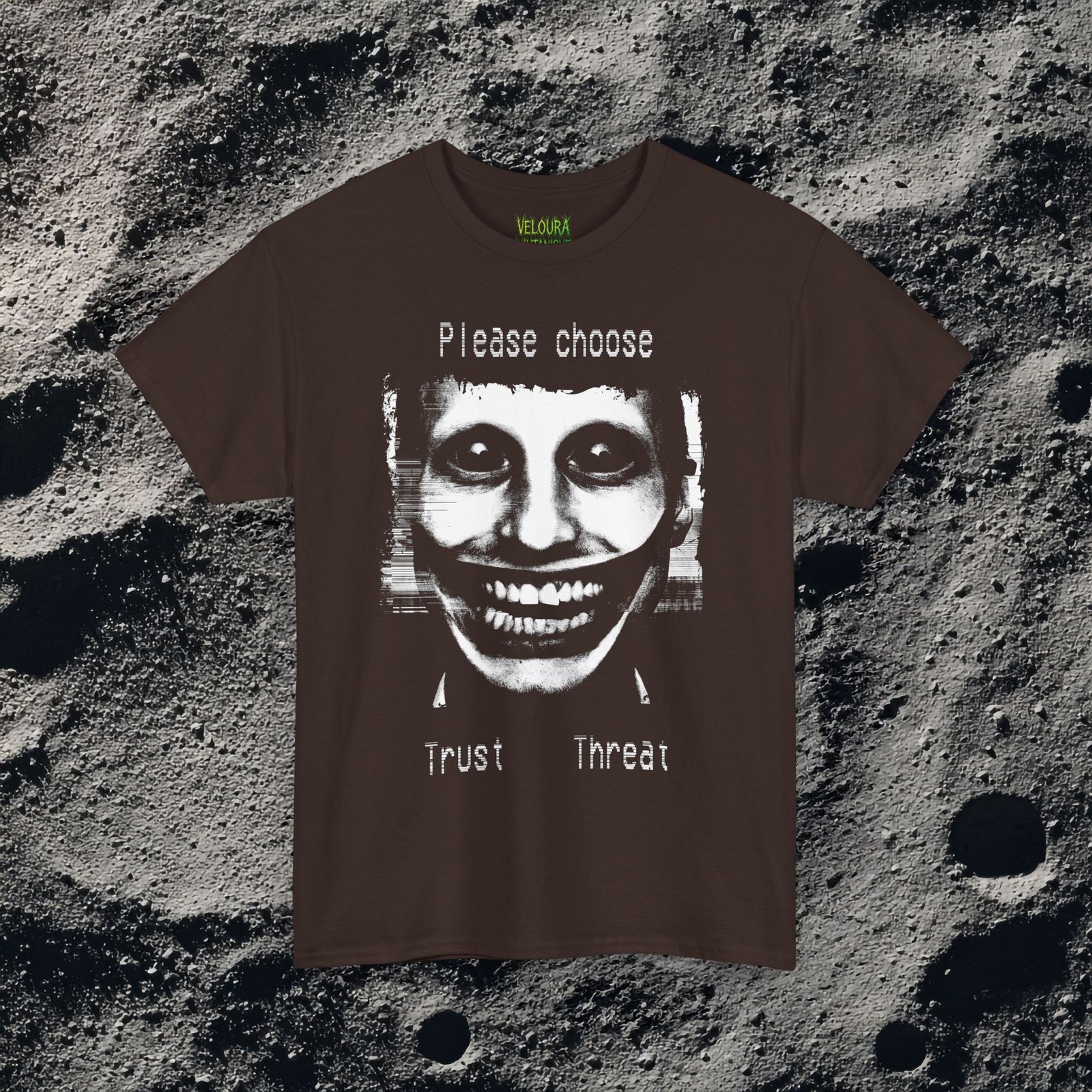 This t-shirt features a disturbing analog horror design of a grinning distorted face in black and white, wide staring eyes, unnaturally stretched mouth filled with teeth, glitch effects across the image. Above the figure is the phrase "Please choose," and below are the words "Trust" and "Threat," giving the design a psychological horror aesthetic that feels like a warning from a cursed VHS tape.