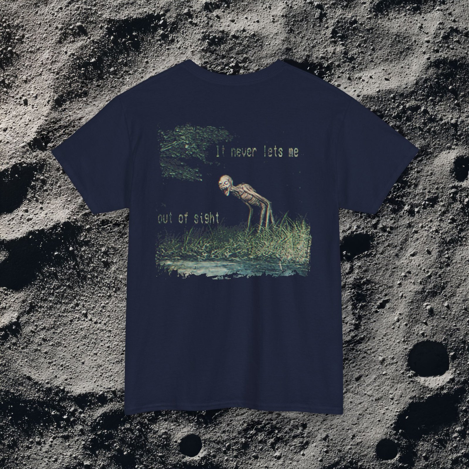 t-shirt features a haunting analog horror design, with the front displaying eerie VHS-style forest imagery and glitch effects alongside the unsettling text “I don’t remember the last time I was alone,” while the back shows a grainy night scene of tall grass and trees with a distorted, skeletal humanoid creature leaning forward and staring with a wide grin, accompanied by the chilling phrase “It never lets me out of sight,” creating a disturbing and atmospheric look that captures the feeling of being stalked and never truly alone.