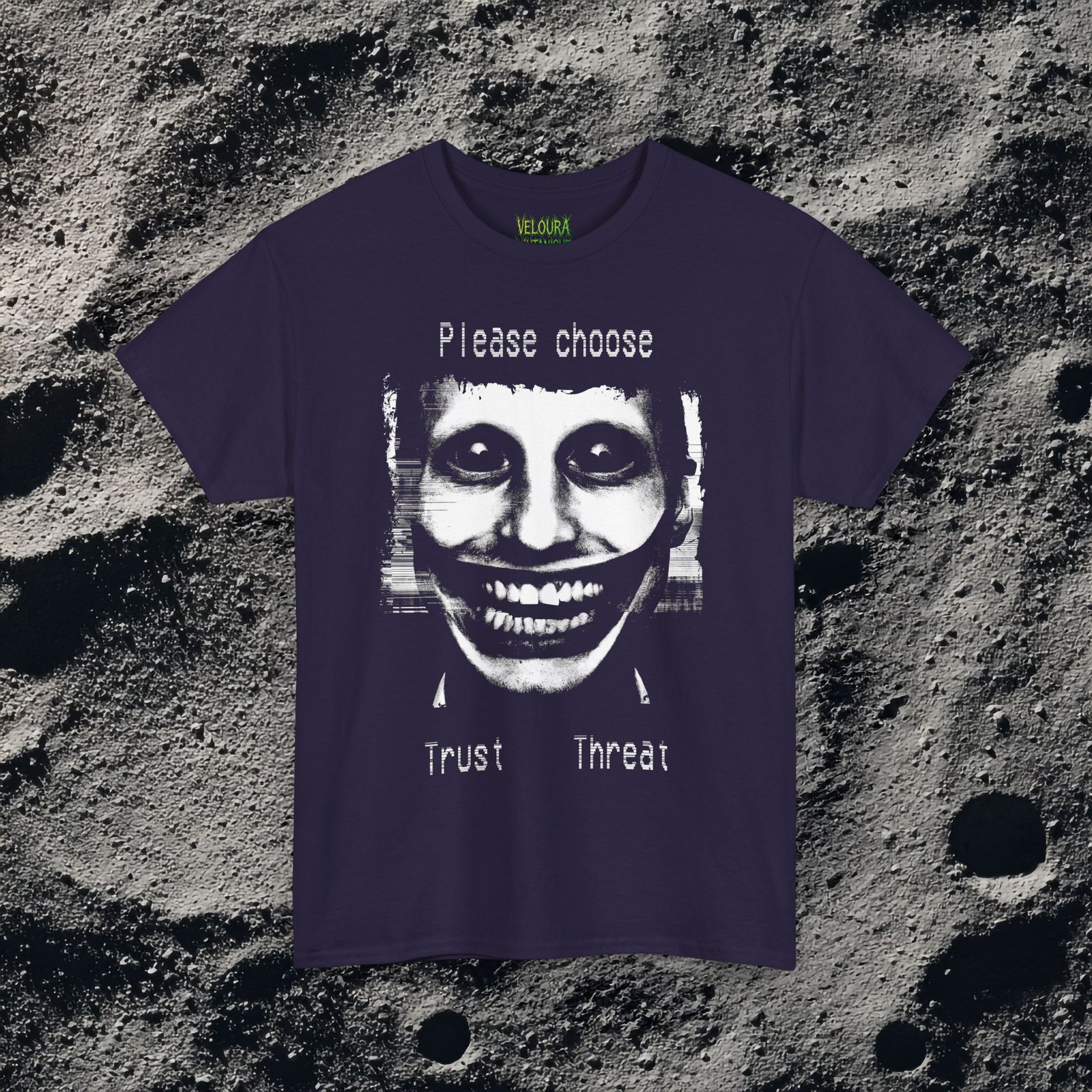 This t-shirt features a disturbing analog horror design of a grinning distorted face in black and white, wide staring eyes, unnaturally stretched mouth filled with teeth, glitch effects across the image. Above the figure is the phrase "Please choose," and below are the words "Trust" and "Threat," giving the design a psychological horror aesthetic that feels like a warning from a cursed VHS tape.