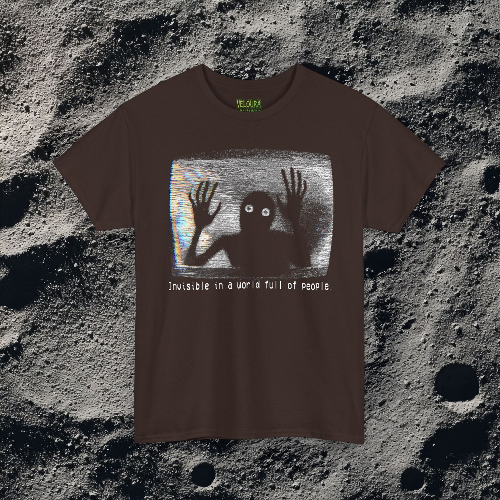 This black T-shirt features an analog horror inspired design of a grainy, distorted humanoid silhouette trapped inside a static-filled television screen. The shadowy figure presses its long, bony hands against the glass as if trying to escape, while its glowing white eyes stare outward in a mix of fear and desperation. VHS-style static and rainbow glitch streaks fill the background, giving the design the appearance of a corrupted video frame. Beneath the image, in a pixelated glitch font, the text reads “Invisible in a world full of people,” adding a dark, emotional layer of loneliness and isolation to the already unsettling graphic.