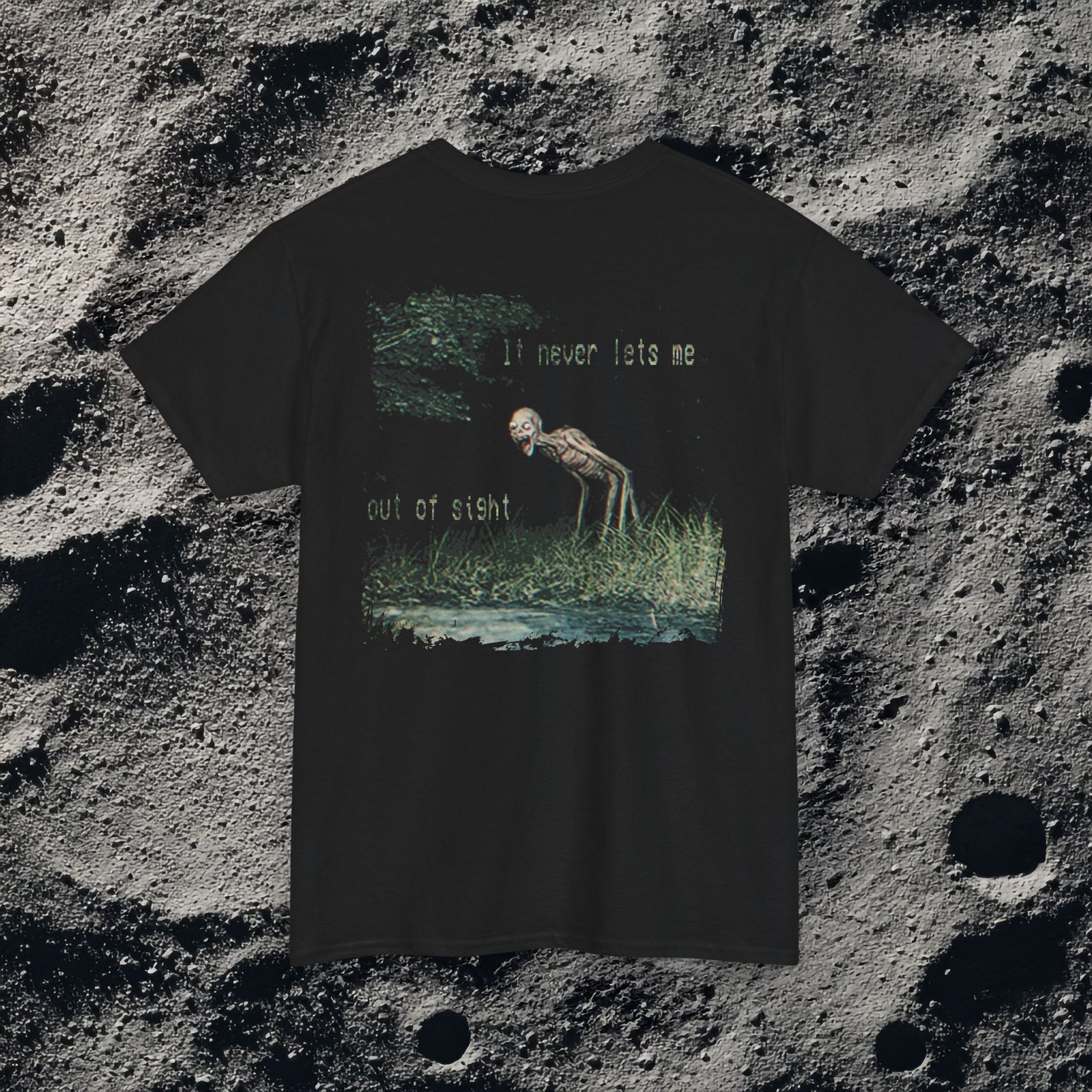 t-shirt features a haunting analog horror design, with the front displaying eerie VHS-style forest imagery and glitch effects alongside the unsettling text “I don’t remember the last time I was alone,” while the back shows a grainy night scene of tall grass and trees with a distorted, skeletal humanoid creature leaning forward and staring with a wide grin, accompanied by the chilling phrase “It never lets me out of sight,” creating a disturbing and atmospheric look that captures the feeling of being stalked and never truly alone.