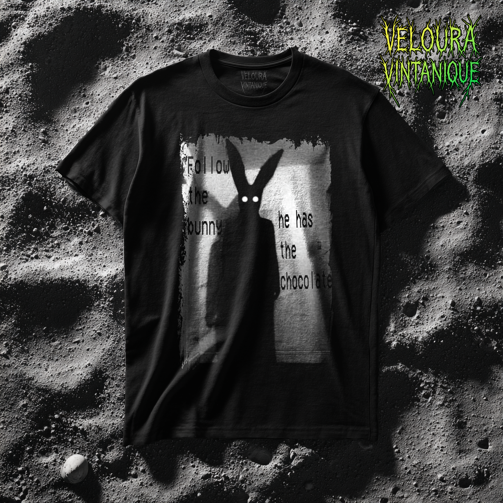 This black t-shirt displays a haunting analog horror-inspired design in grainy black and white. At the center stands a tall shadowy humanoid figure with unnaturally long rabbit ears and glowing white eyes. The eerie background resembles a dimly lit corridor, adding to the unsettling atmosphere. Surrounding the figure, distorted text reads “Follow the bunny, he has the chocolate”, blending a playful Easter phrase with a chilling, horror aesthetic.