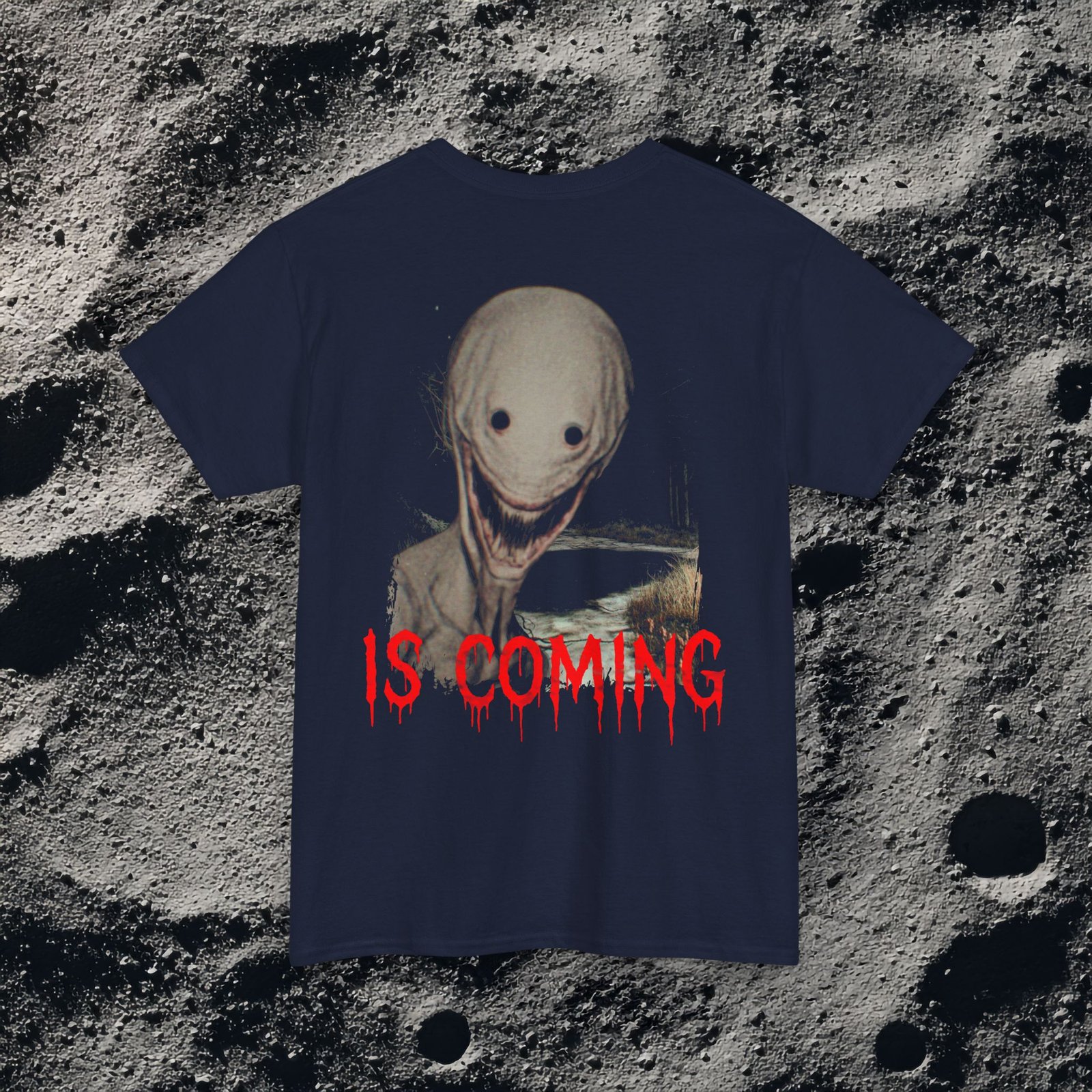 The shirt features a dark, desaturated forest path surrounded by dead trees and heavy shadows, creating a cold, abandoned atmosphere. Above the scene, dripping red text reads “THE FOG,” while on the opposite side a distorted, pale humanoid creature with hollow eyes and a wide, unnatural smile emerges from the misty background. Beneath it, the matching red text “IS COMING” completes the ominous analog-horror design.