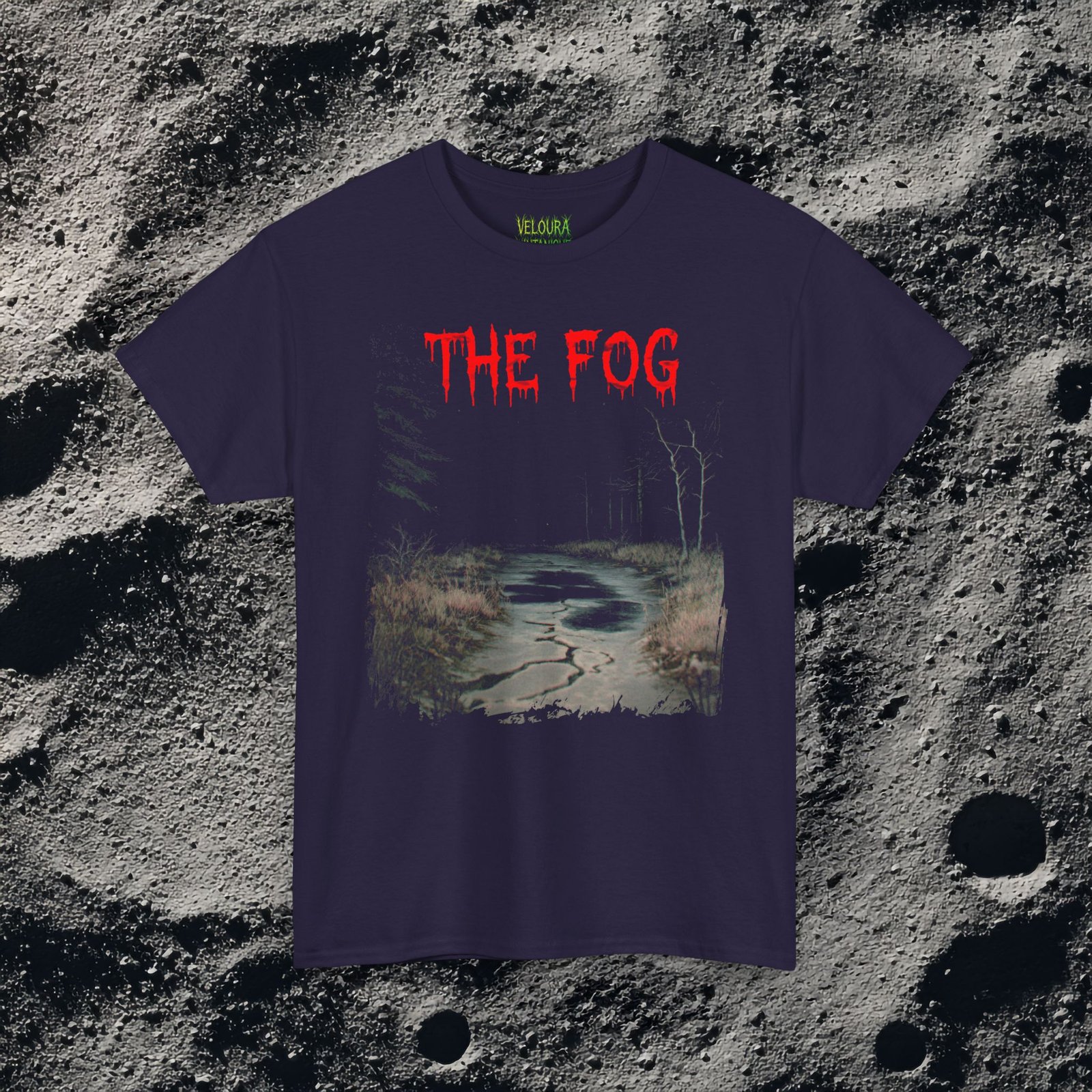 The shirt features a dark, desaturated forest path surrounded by dead trees and heavy shadows, creating a cold, abandoned atmosphere. Above the scene, dripping red text reads “THE FOG,” while on the opposite side a distorted, pale humanoid creature with hollow eyes and a wide, unnatural smile emerges from the misty background. Beneath it, the matching red text “IS COMING” completes the ominous analog-horror design.
