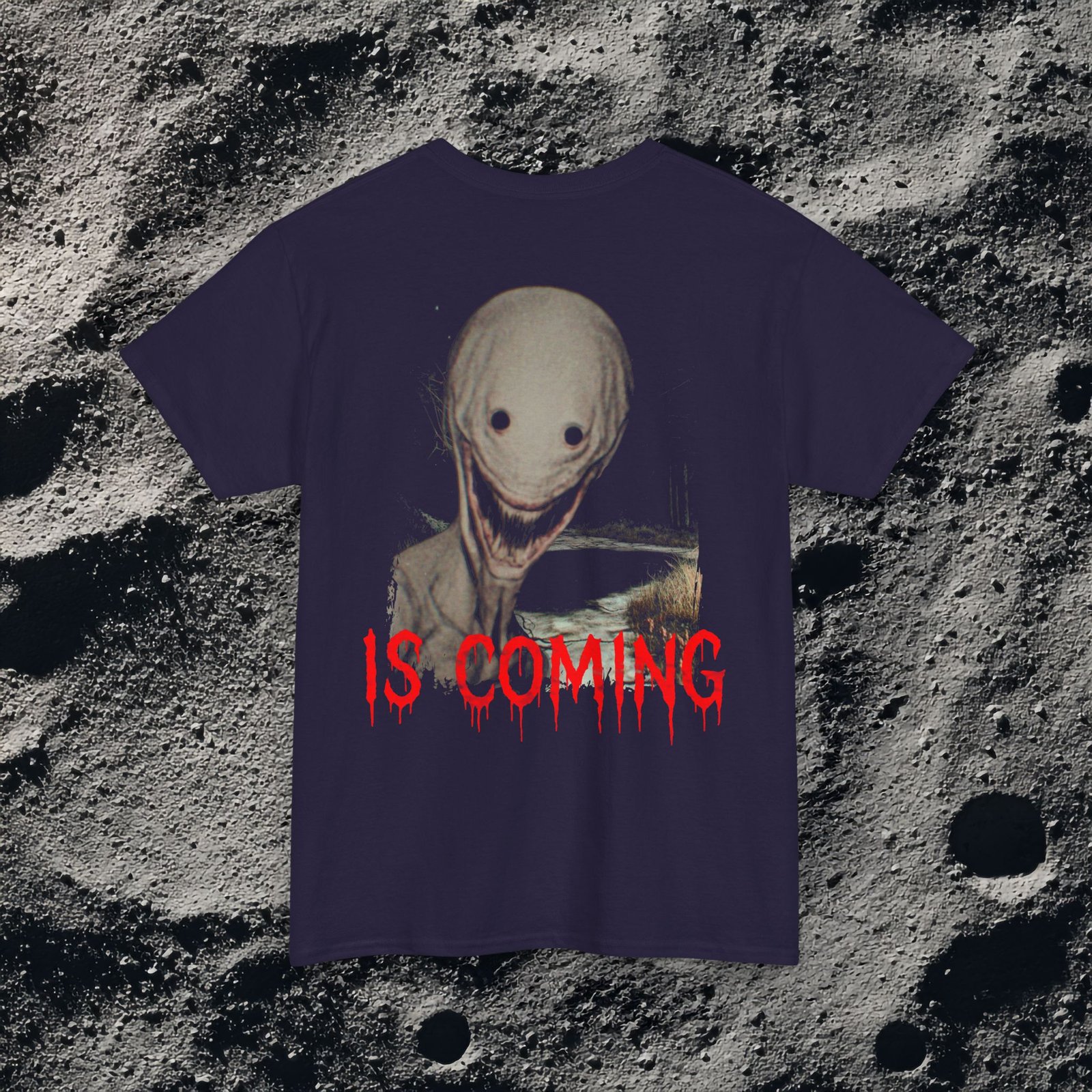 The shirt features a dark, desaturated forest path surrounded by dead trees and heavy shadows, creating a cold, abandoned atmosphere. Above the scene, dripping red text reads “THE FOG,” while on the opposite side a distorted, pale humanoid creature with hollow eyes and a wide, unnatural smile emerges from the misty background. Beneath it, the matching red text “IS COMING” completes the ominous analog-horror design.