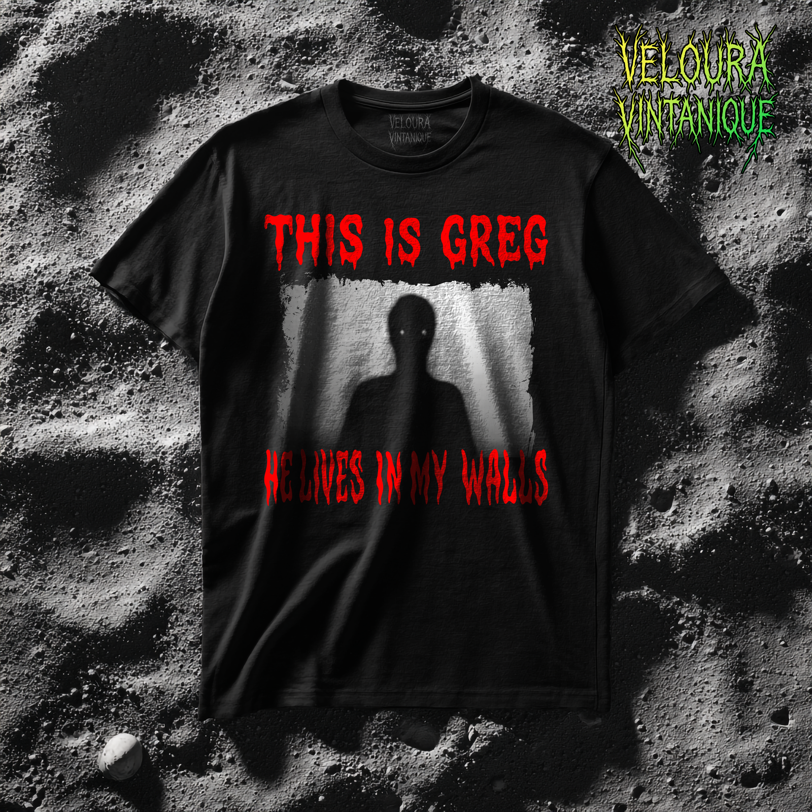 The shirt features a distorted, grainy black-and-white image of a tall, shadowy humanoid figure standing behind what looks like a wrinkled curtain or textured fabric. The figure’s eyes glow as two small white dots, creating an unsettling focal point in the center of the design. Above the image, the phrase “THIS IS GREG” is written in large, dripping red horror-style lettering. Beneath the image, the matching red text “HE LIVES IN MY WALLS” appears in the same melting font. The overall composition creates an eerie analog-horror aesthetic with the dark silhouette, rough texture, and vivid blood-red typography.