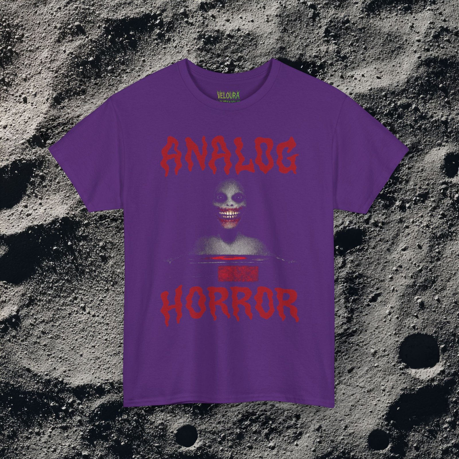 This T-shirt features a disturbing analog horror design with a shadowy smiling figure emerging from darkness, framed by bold dripping red ANALOG HORROR text. The grainy texture, low-contrast lighting, and VHS-style distortion create the feeling of a cursed tape still playing long after it should have stopped. The unsettling grin and minimal color palette amplify the psychological horror aesthetic, making this shirt perfect for fans of analog horror, creepypasta, liminal media, and retro VHS nightmares.