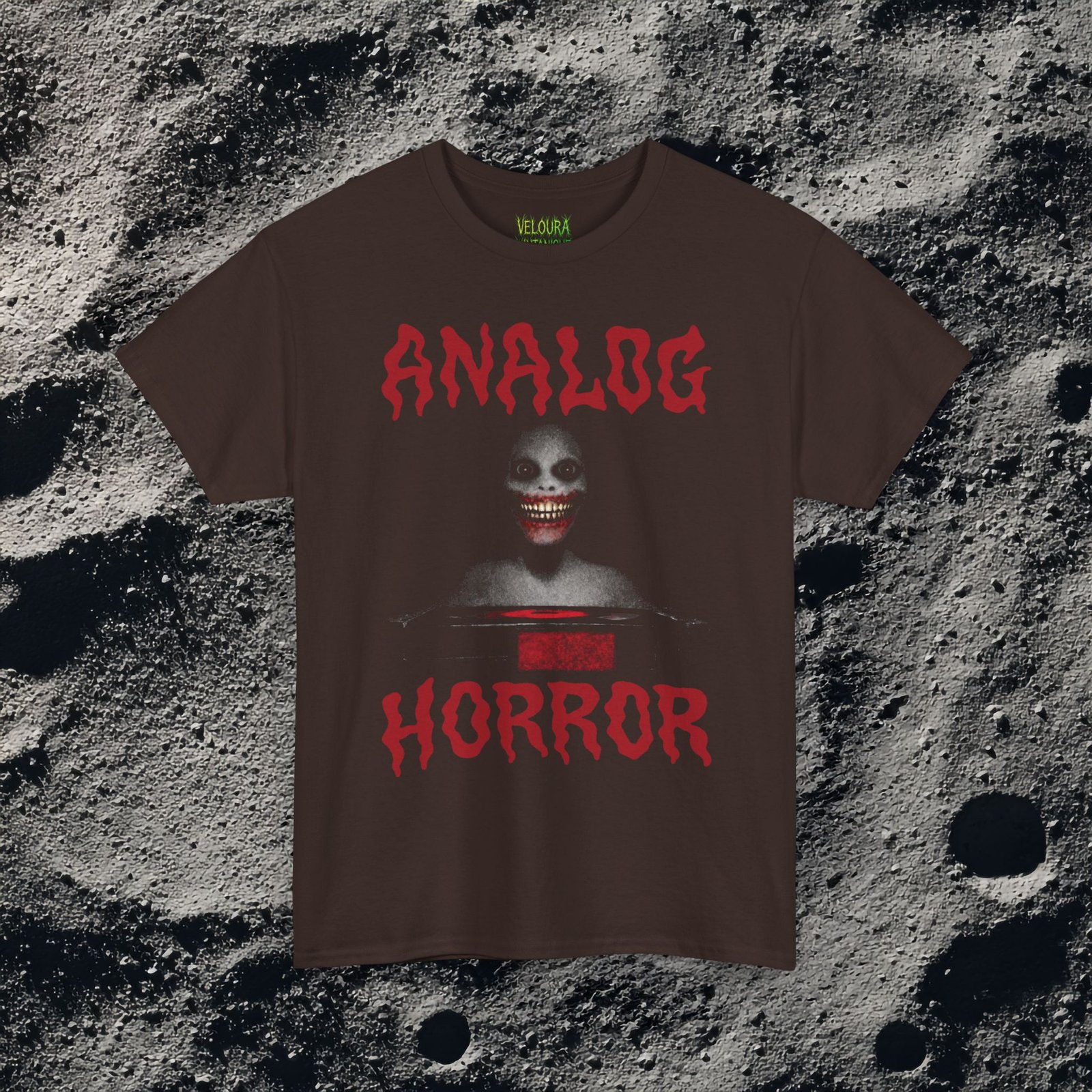 This T-shirt features a disturbing analog horror design with a shadowy smiling figure emerging from darkness, framed by bold dripping red ANALOG HORROR text. The grainy texture, low-contrast lighting, and VHS-style distortion create the feeling of a cursed tape still playing long after it should have stopped. The unsettling grin and minimal color palette amplify the psychological horror aesthetic, making this shirt perfect for fans of analog horror, creepypasta, liminal media, and retro VHS nightmares.