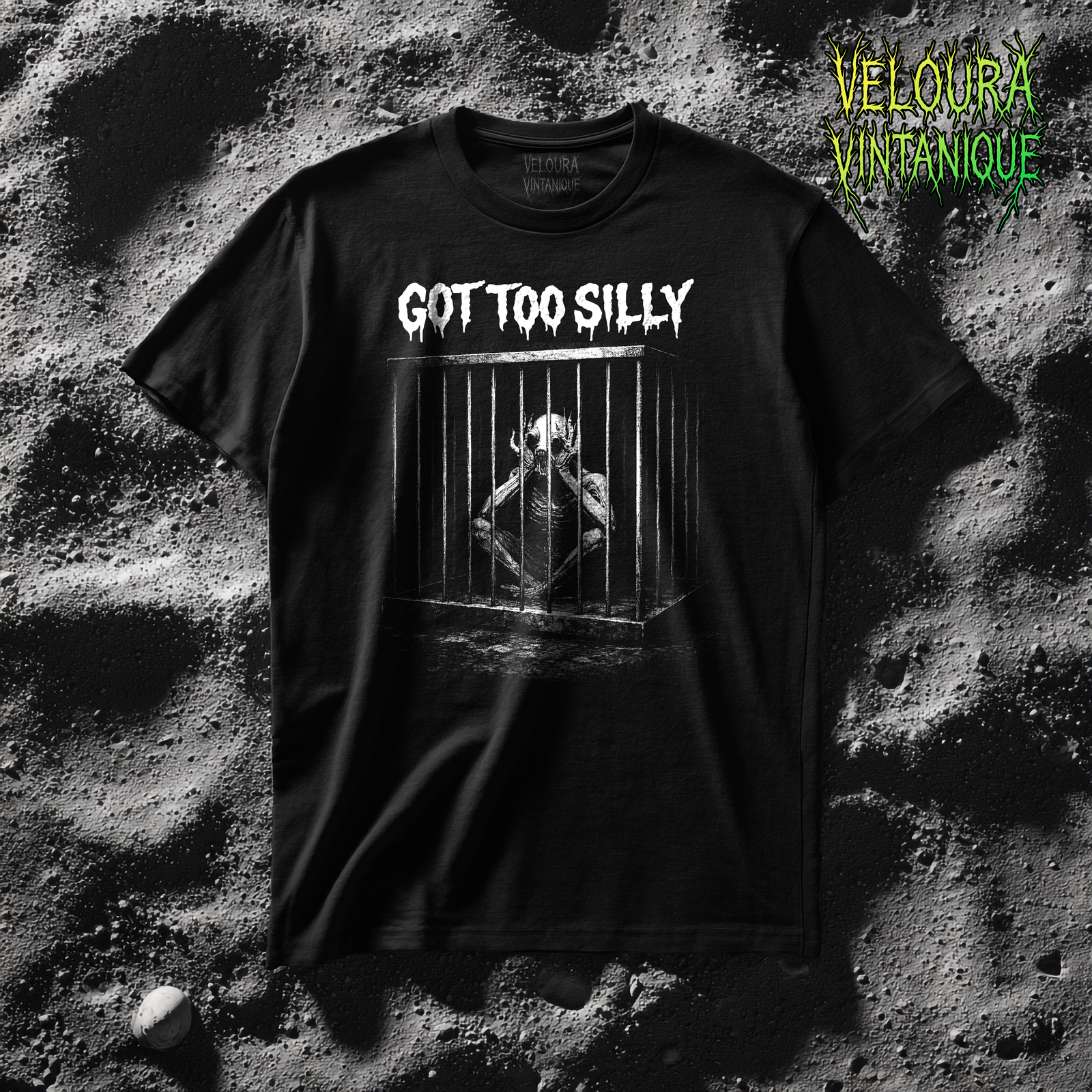 This T-shirt features a haunting black-and-white illustration of a skeletal, creature-like figure crouched inside a metal cage, paired with the unsettling phrase “Got Too Silly.” The contrast between the playful wording and the grim imagery creates a powerful piece of dark humor. Inspired by horror art, gothic illustration, and surreal absurdism, the design evokes themes of confinement, madness, and irony. A perfect statement shirt for fans of creepy art, underground horror, and ironic graphic tees.