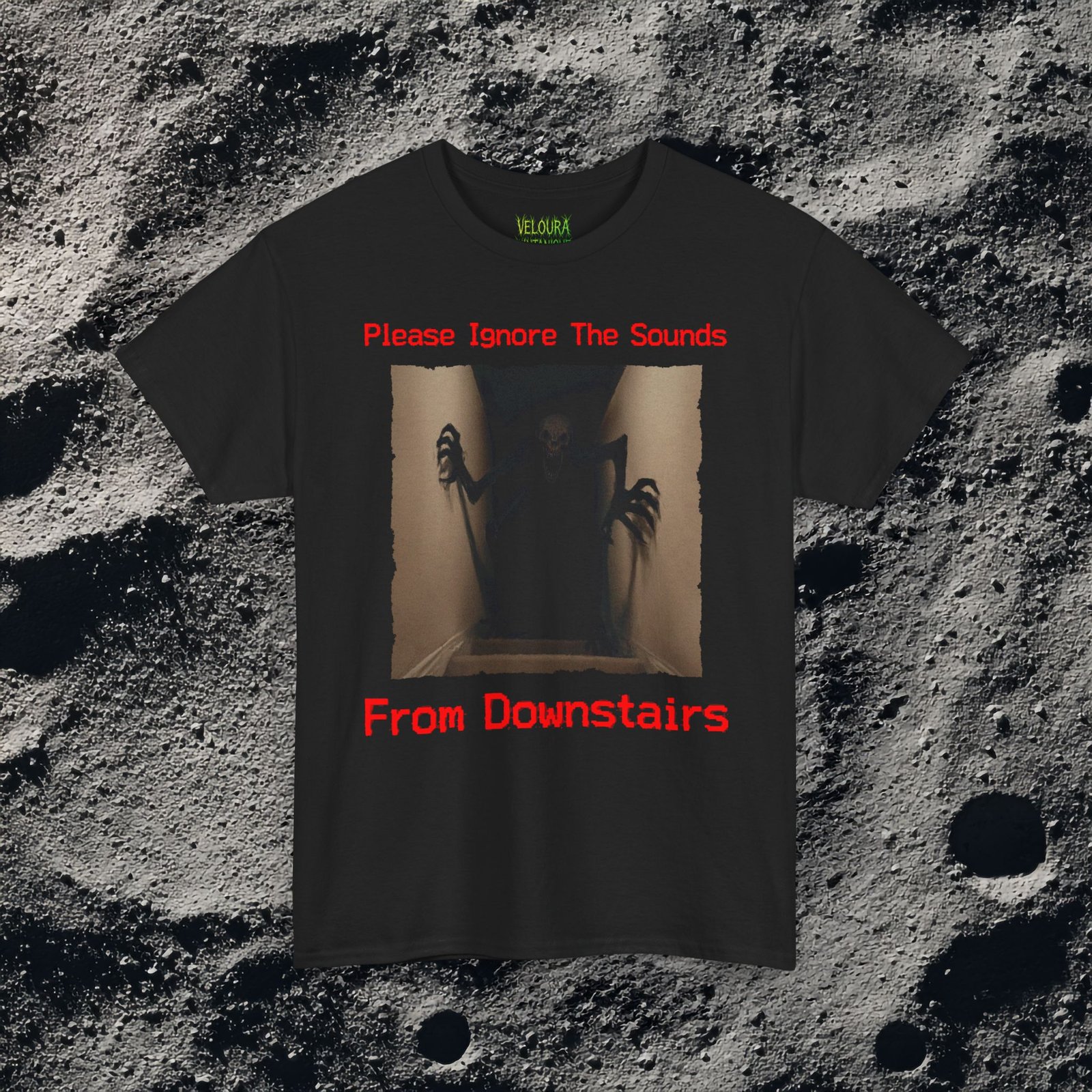 This horror-inspired T-shirt features a terrifying shadow creature crawling up from a dark basement stairwell, framed in dim lighting with an unsettling atmosphere. The bold red text reads, “Please Ignore The Sounds From Downstairs,” adding a disturbing, analog horror tone to the artwork. The creature’s elongated limbs and sharp claws create a nightmarish silhouette that stands out on black fabric. Perfect for horror fans, Halloween lovers, creepy aesthetic enthusiasts, and anyone who enjoys dark, unsettling graphic tees.