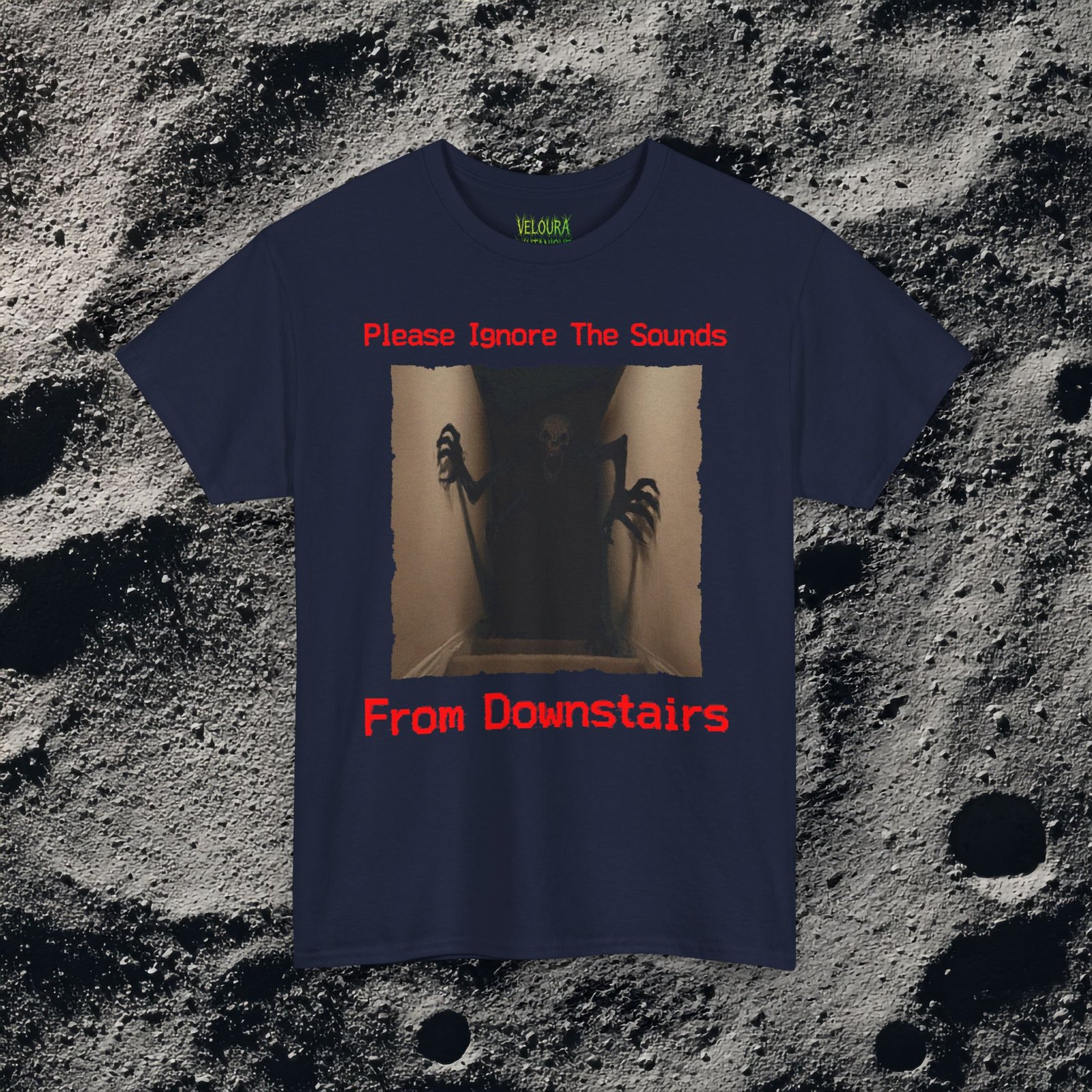 This horror-inspired T-shirt features a terrifying shadow creature crawling up from a dark basement stairwell, framed in dim lighting with an unsettling atmosphere. The bold red text reads, “Please Ignore The Sounds From Downstairs,” adding a disturbing, analog horror tone to the artwork. The creature’s elongated limbs and sharp claws create a nightmarish silhouette that stands out on black fabric. Perfect for horror fans, Halloween lovers, creepy aesthetic enthusiasts, and anyone who enjoys dark, unsettling graphic tees.
