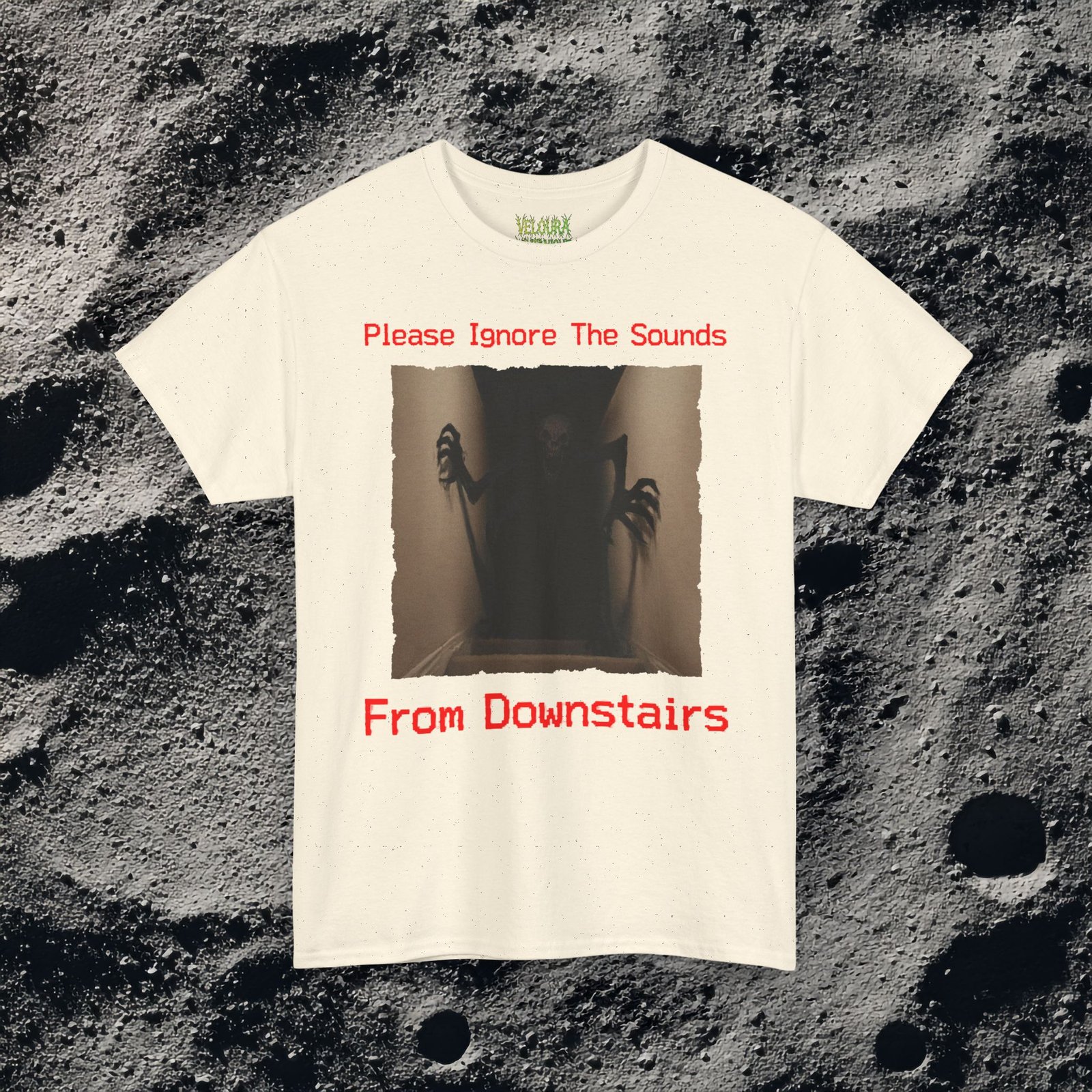 This horror-inspired T-shirt features a terrifying shadow creature crawling up from a dark basement stairwell, framed in dim lighting with an unsettling atmosphere. The bold red text reads, “Please Ignore The Sounds From Downstairs,” adding a disturbing, analog horror tone to the artwork. The creature’s elongated limbs and sharp claws create a nightmarish silhouette that stands out on black fabric. Perfect for horror fans, Halloween lovers, creepy aesthetic enthusiasts, and anyone who enjoys dark, unsettling graphic tees.