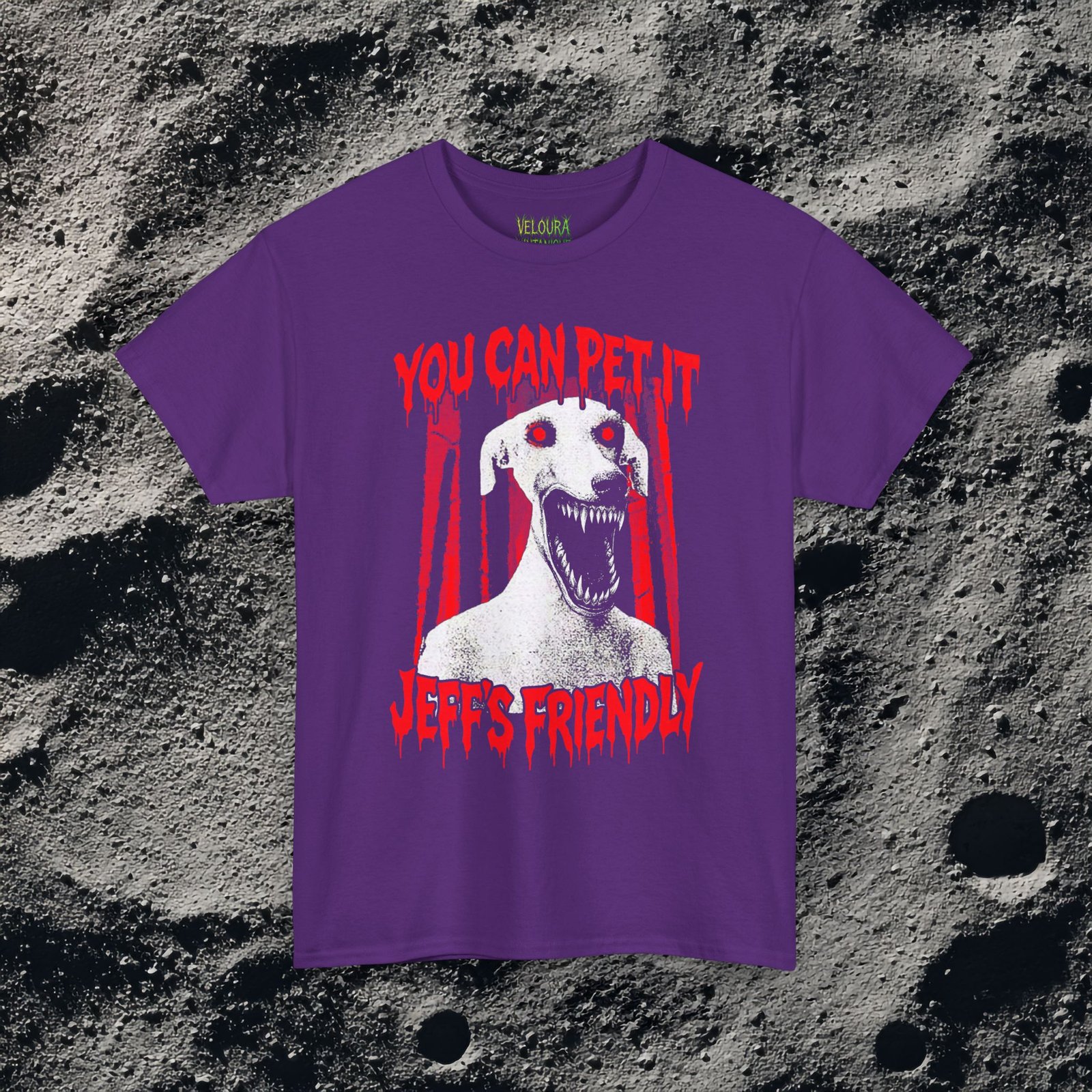 This creepy horror T-shirt features a terrifying dog-like creature with glowing red eyes and a wide mouth full of sharp teeth. The disturbing figure appears against a dark forest background, while dripping red horror-style text reads “YOU CAN PET IT” and “JEFF’S FRIENDLY.” The gritty analog horror art style creates an unsettling atmosphere reminiscent of internet creepypasta and cursed VHS aesthetics. The bold red and black contrast gives the design a striking and sinister look.