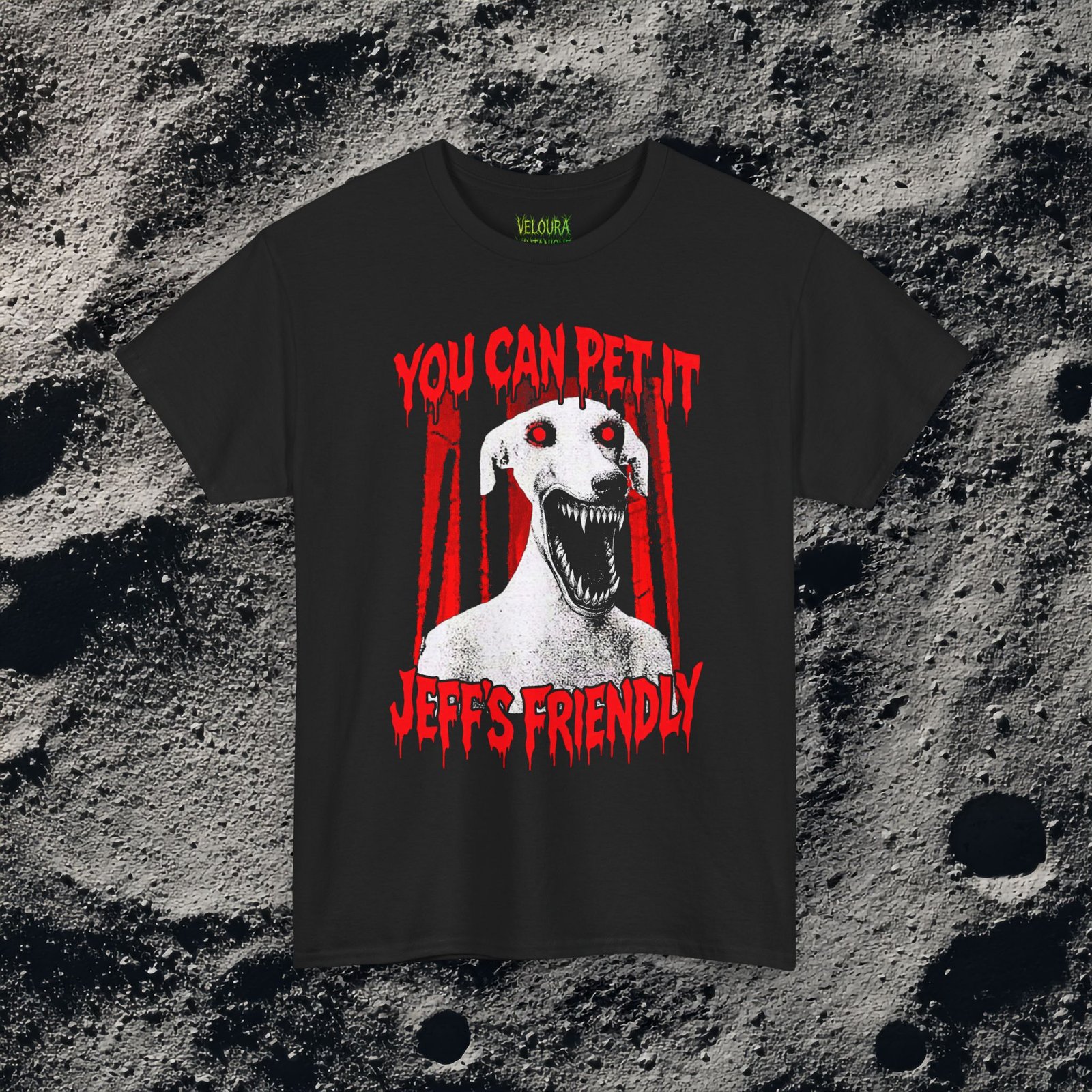 This creepy horror T-shirt features a terrifying dog-like creature with glowing red eyes and a wide mouth full of sharp teeth. The disturbing figure appears against a dark forest background, while dripping red horror-style text reads “YOU CAN PET IT” and “JEFF’S FRIENDLY.” The gritty analog horror art style creates an unsettling atmosphere reminiscent of internet creepypasta and cursed VHS aesthetics. The bold red and black contrast gives the design a striking and sinister look.