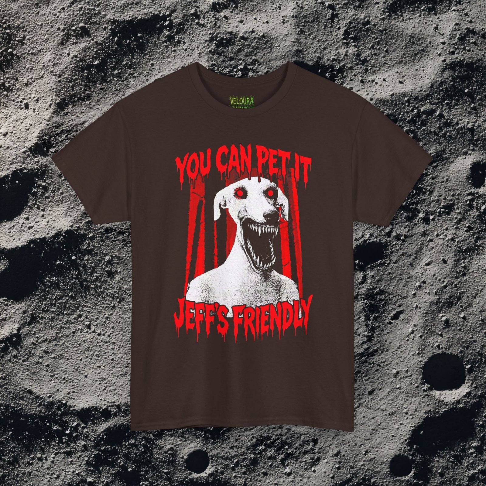 This creepy horror T-shirt features a terrifying dog-like creature with glowing red eyes and a wide mouth full of sharp teeth. The disturbing figure appears against a dark forest background, while dripping red horror-style text reads “YOU CAN PET IT” and “JEFF’S FRIENDLY.” The gritty analog horror art style creates an unsettling atmosphere reminiscent of internet creepypasta and cursed VHS aesthetics. The bold red and black contrast gives the design a striking and sinister look.
